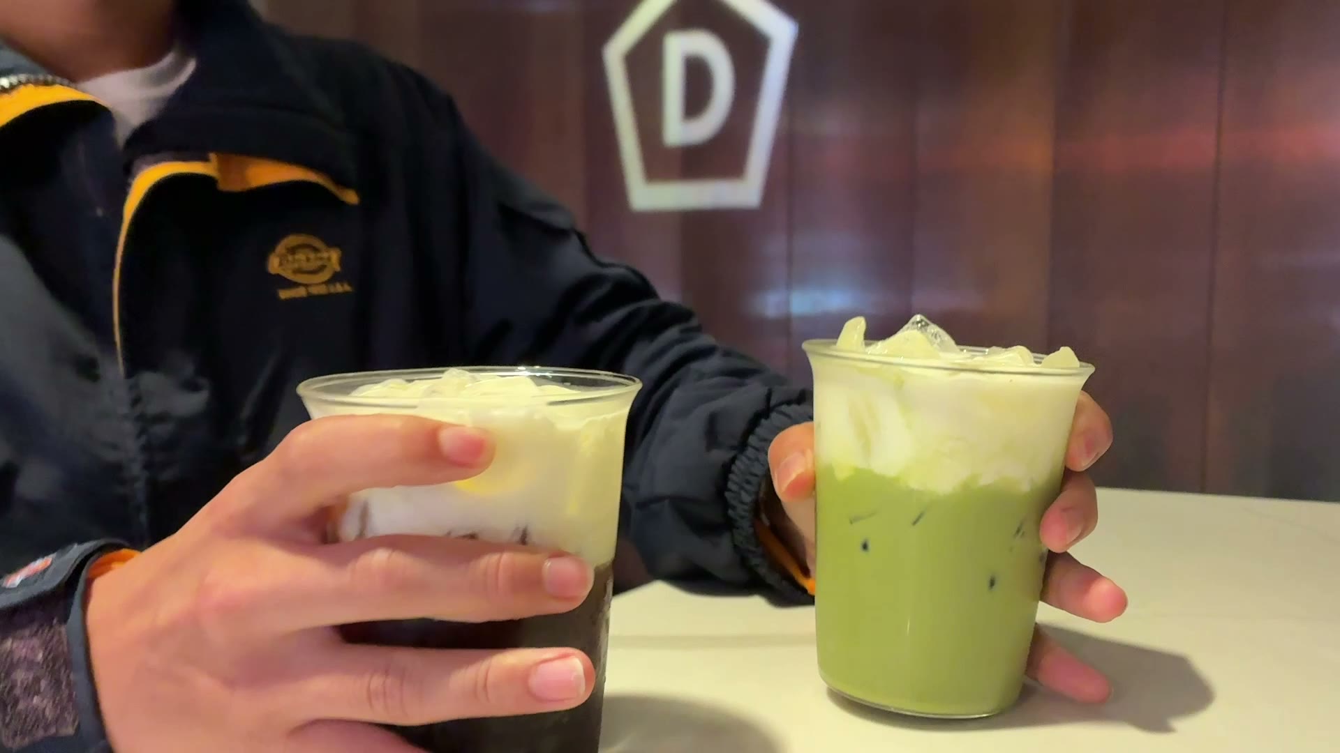 Two signature drinks at Offset x D, a dark cold brew and a green matcha, both topped with coconut cream