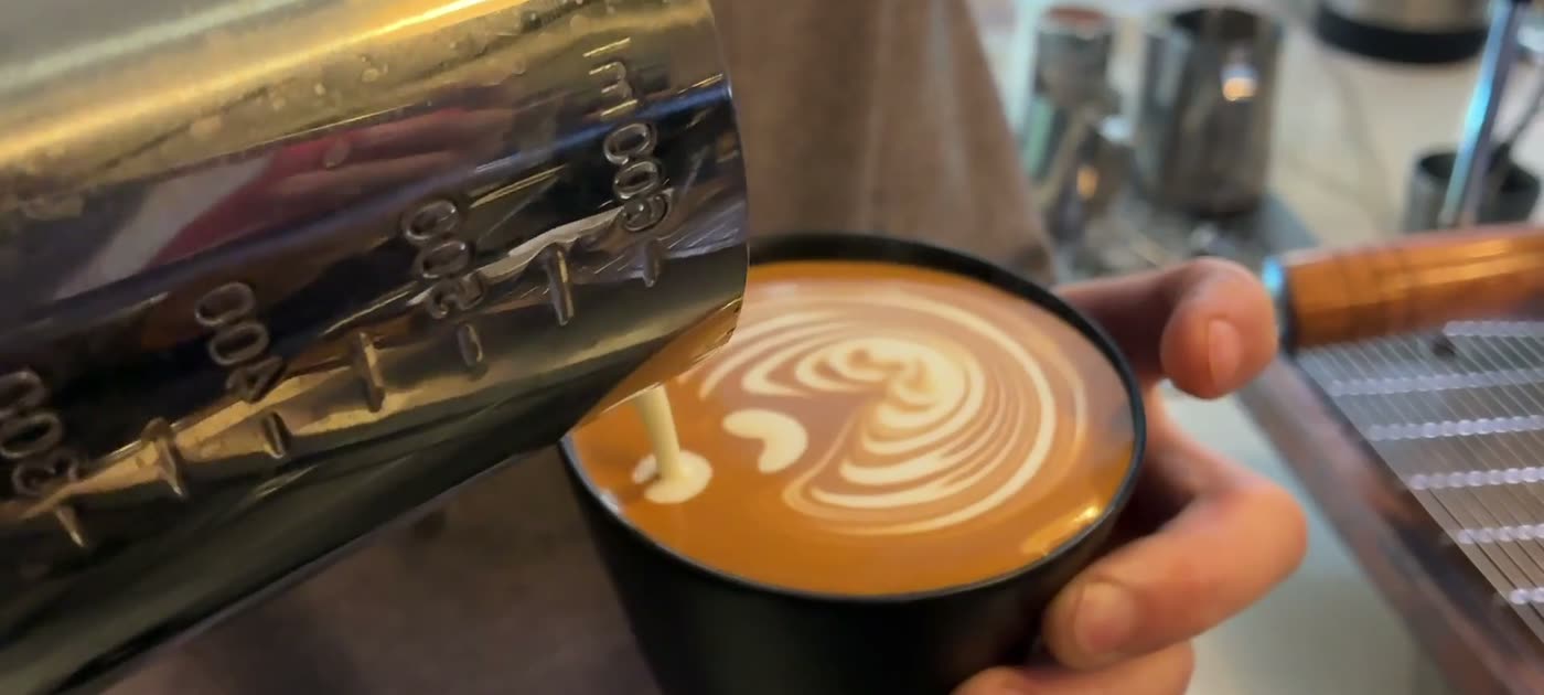 A barista pouring latte art into a black cup at the Offset bar