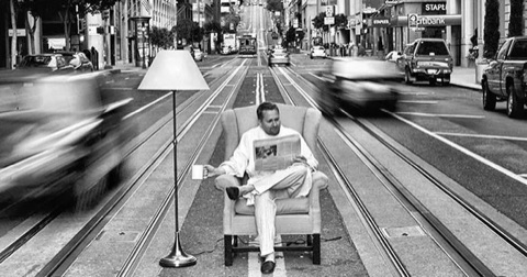 A man reading the newspaper in an armchair in the middle of a busy street